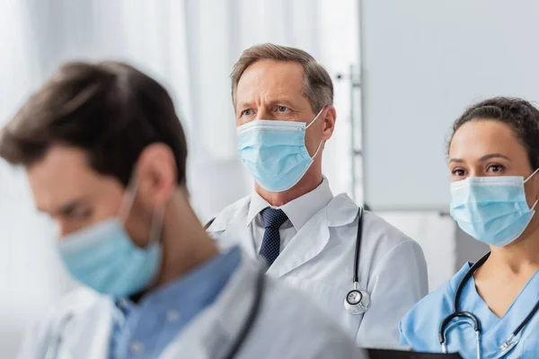 의료용 마스크를 민족의 의사와 간호사가 앞쪽에서 동료와 만나는 시선을 돌리고 — 스톡 사진