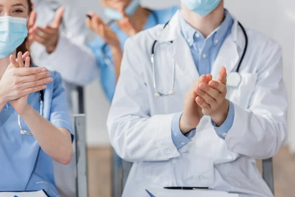 病院の会議中にぼやけた背景で拍手する医療マスクの病院スタッフ — ストック写真