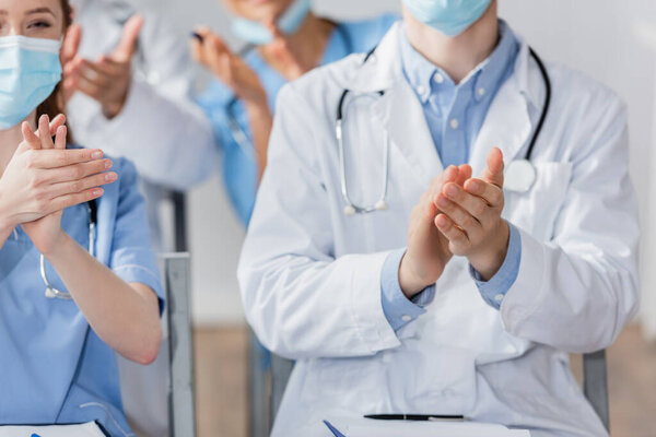 Hospital staff in medical masks applauding during meeting in hospital on blurred background