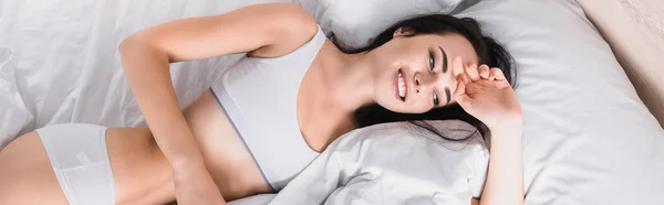 ベッドに横たわっている下着姿で若いブルネットの女性を笑顔のトップビュー バナー — ストック写真