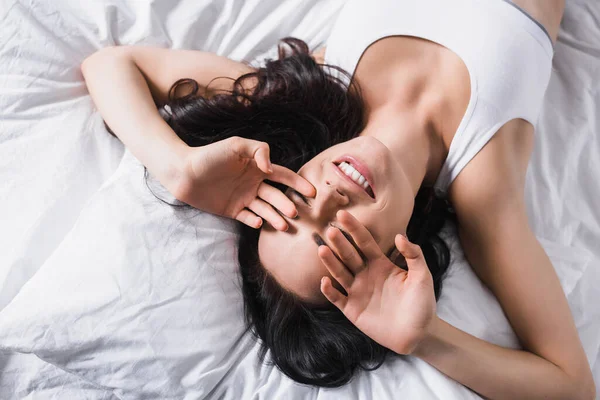 若い笑顔のブルネットの女性がベッドの上に横たわっている — ストック写真