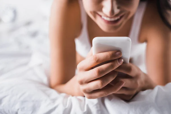 스마트폰을 사용하여 침대에 미소짓고 여자의 — 스톡 사진
