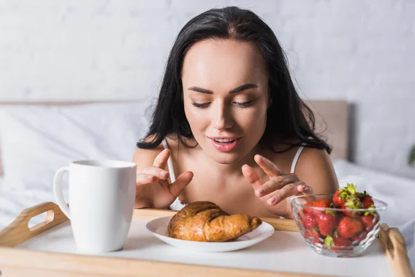 Nuori Brunette Nainen Ottaa Croissant Mansikka Kaakao Aamiaiseksi Sängyssä — kuvapankkivalokuva