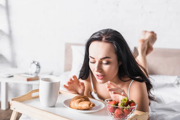 Nuori Brunette Nainen Ottaa Croissant Mansikka Kaakao Aamiaiseksi Sängyssä — kuvapankkivalokuva