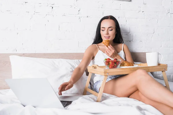 Sonriente Joven Morena Mujer Desayunando Cama Mientras Usa Ordenador Portátil — Foto de Stock