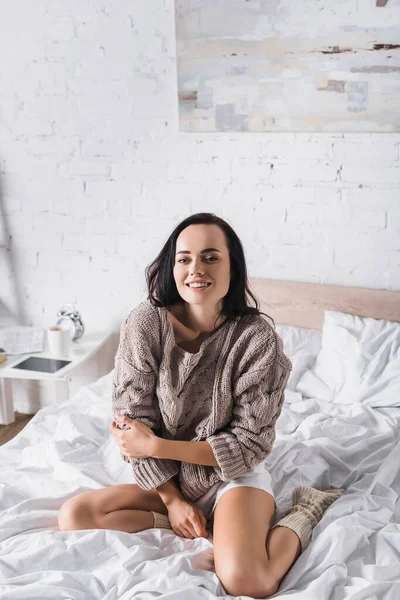 幸せな若いですブルネット女性でセーターと靴下でベッドに座って朝 — ストック写真