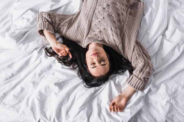 top view of young brunette woman in sweater sleeping in bed at morning