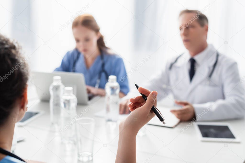 African american nurse holding pen near colleagues on blurred background in clinic 