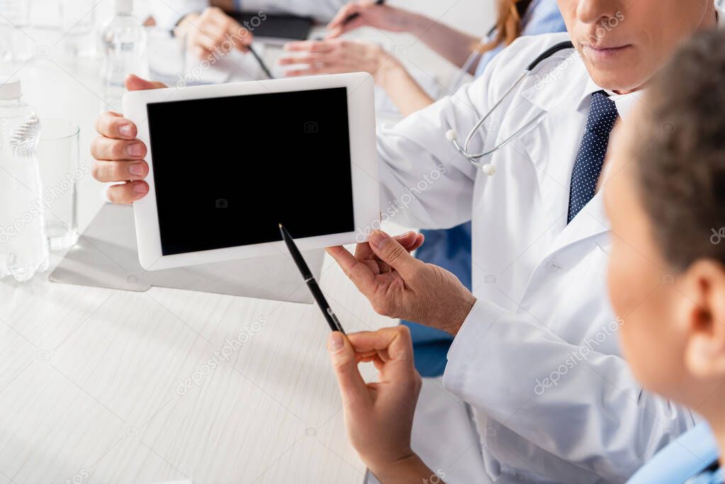 African american nurse pointing at digital tablet with blank screen near doctor and colleagues on blurred background 