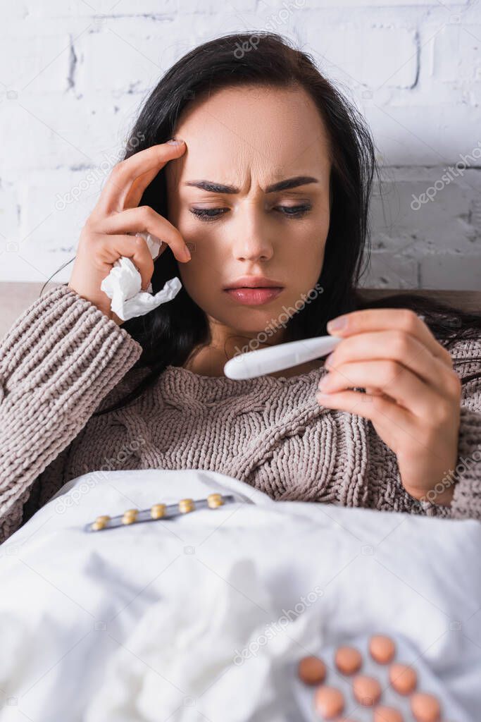 sick young brunette woman with tissue and thermometer in bed