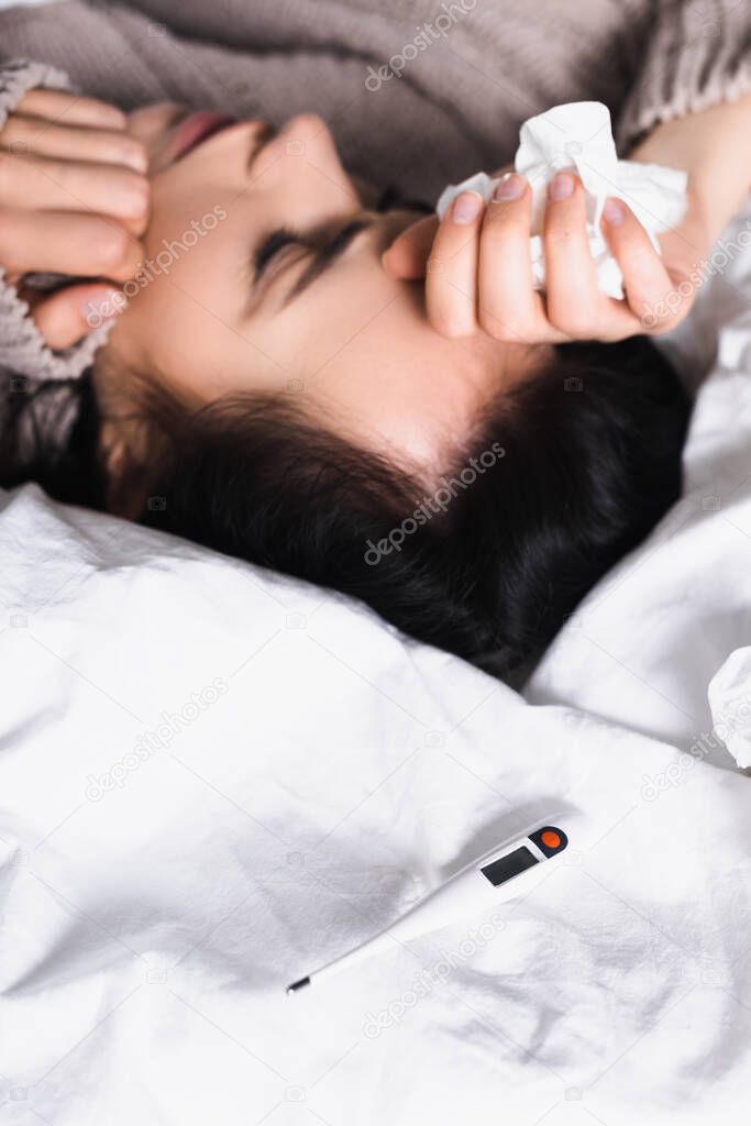 sick young brunette woman with thermometer and tissue in bed