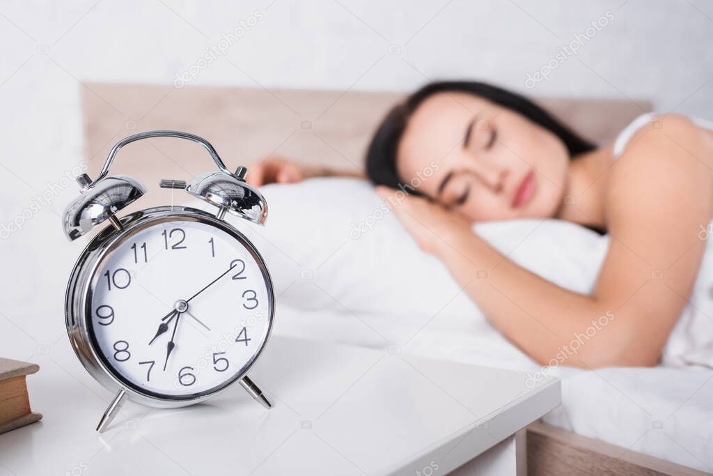 classic alarm clock and blurred young brunette woman sleeping in bed on background