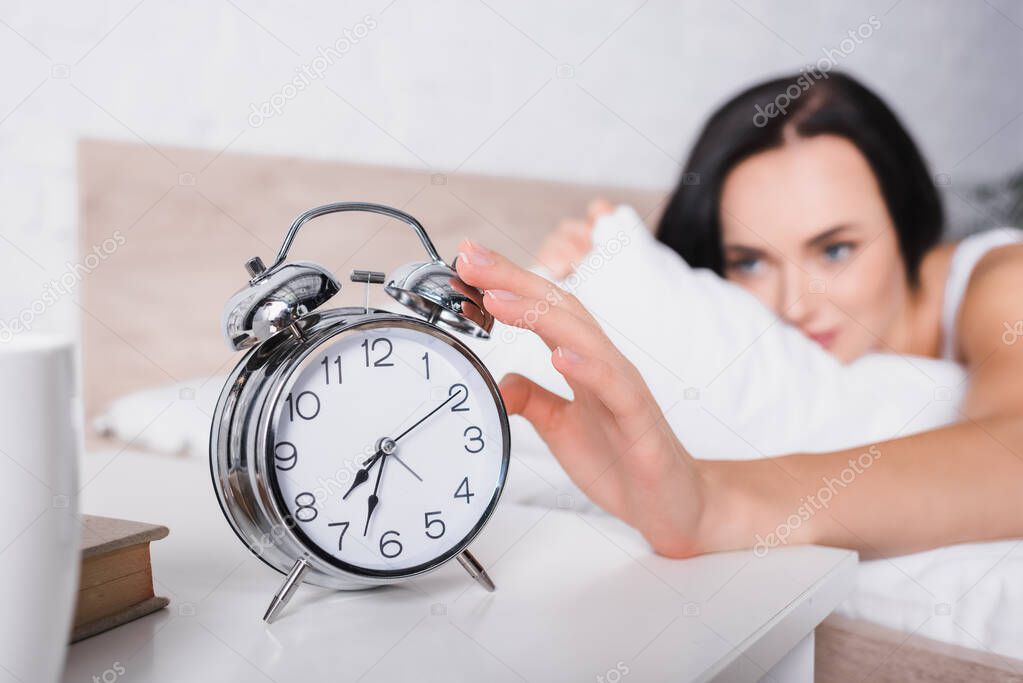 classic alarm clock and blurred young brunette woman in bed on background