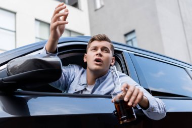 drunk, angry man with bottle of whiskey shouting while looking out car window clipart