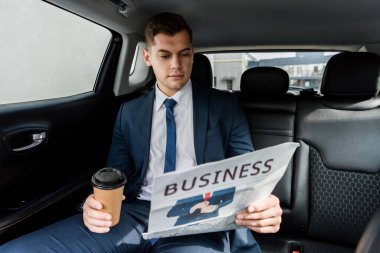 Young businessman holding coffee to go and reading news on blurred foreground in car clipart