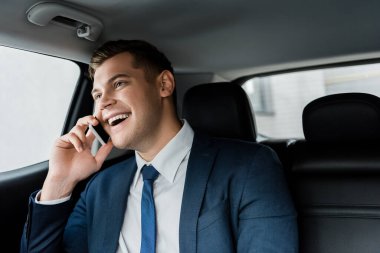 Neşeli yönetici otomobilin arka koltuğunda akıllı telefondan konuşuyor.