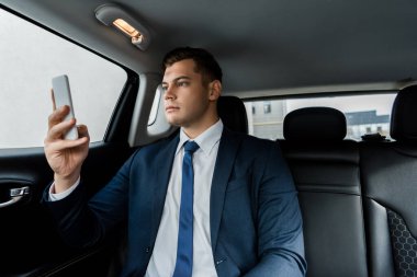 Takım elbiseli genç işadamı otomatikte cep telefonu kullanıyor.