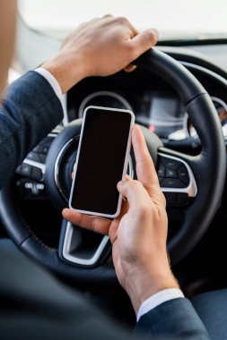 Bulanık arka planda araba sürerken akıllı telefonu boş ekran ile tutan işadamının kırpılmış görüntüsü