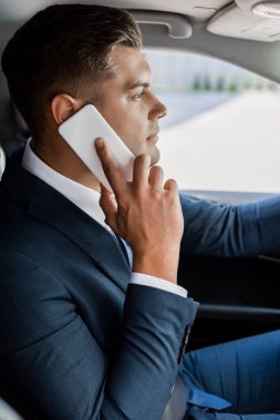 Genç işadamı arka planda otomobille akıllı telefondan konuşuyor.