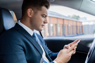 İş adamı arabada sürücü koltuğunda otururken akıllı telefon kullanıyor.