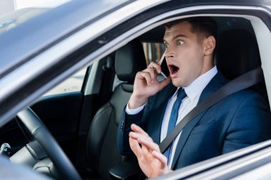 Korkak işadamı, arabanın koltuğunda akıllı telefonla konuşuyor.