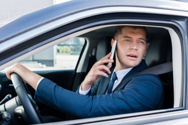 İş adamı araba sürerken pencereye bakıyor ve akıllı telefondan konuşuyor.