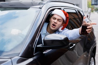 Sarhoş, kızgın, Noel Baba şapkalı, elinde viski şişesi olan, araba sürerken pencereden bakan adam.