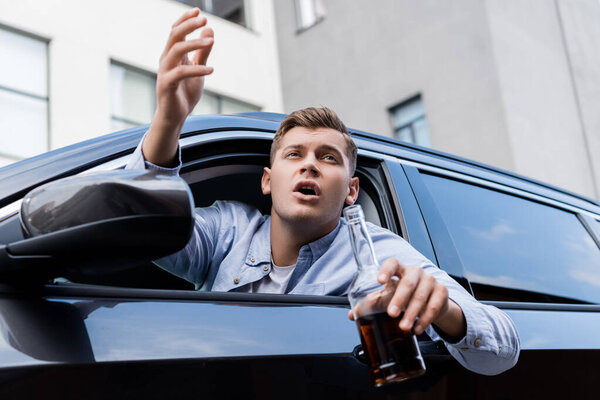 пьяный, злой мужчина с бутылкой виски, кричащий, глядя в окно машины