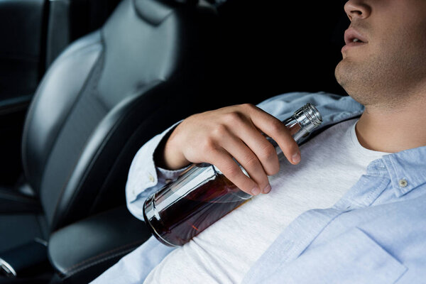частичный вид пьяного мужчины, спящего с бутылкой алкоголя на водительском сидении в машине