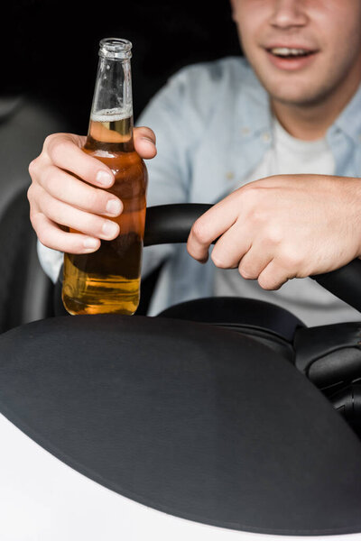 частичный вид пьяного мужчины, держащего бутылку виски за рулем автомобиля, размытый фон