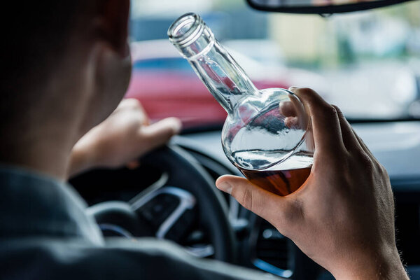 обрезанный вид человека, держащего бутылку алкоголя во время вождения автомобиля, размытый передний план