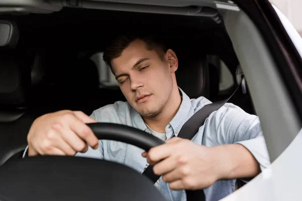 drunk man falling asleep while driving car, blurred foreground