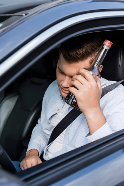 目を閉じたまま車の中に座って酒を飲んでいた男が頭の近くにウイスキーを持っていた — ストック写真