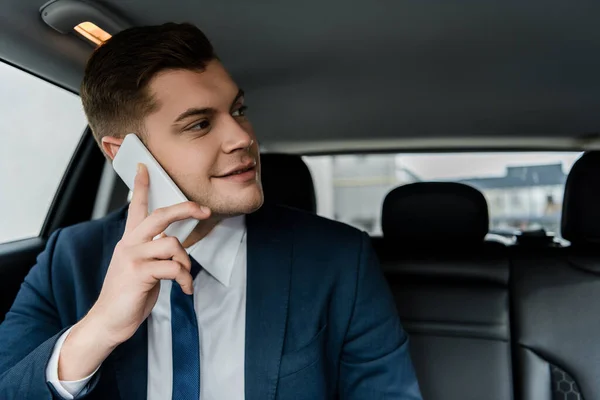 在模糊的背景下 坐在车后座上用手机交谈的笑脸商人 — 图库照片