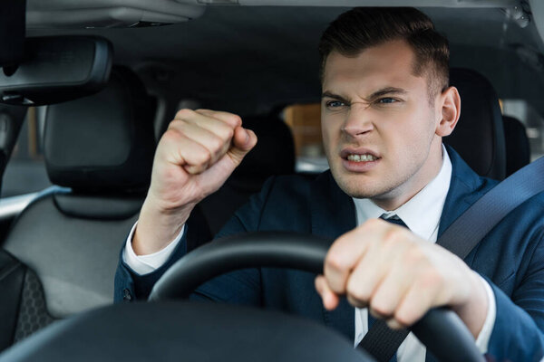 Angry businessman showing fist while driving auto on blurred foreground