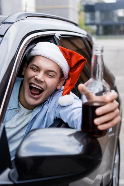 Opilý Muž Santa Klobouk Šklebí Drží Láhev Whisky Autě Rozmazané — Stock fotografie