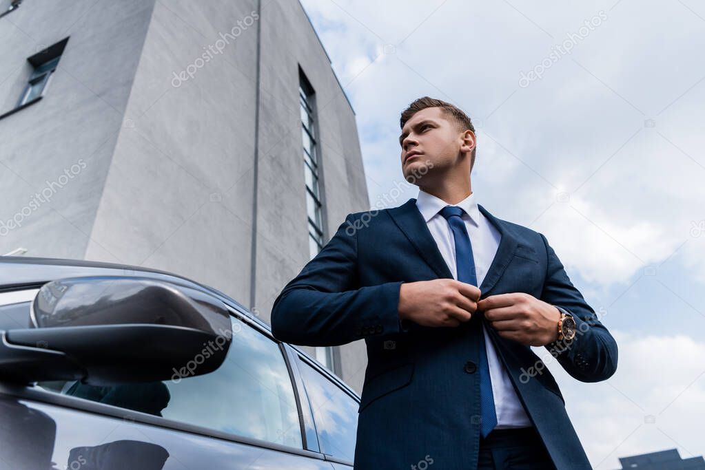 low angle view of businessman buttoning up blazer near car