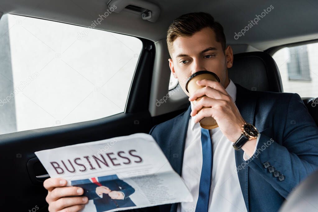 Businessman drinking takeaway coffee and reading newspaper in car