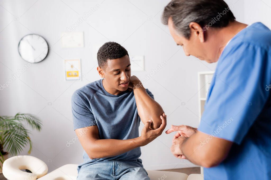 injured african american man showing elbow to doctor in clinic