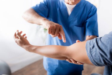 Klinikteki Afrikalı Amerikalı bir adamın yaralı koluna parmağıyla işaret eden kayropraktik uzmanının kırpılmış görüntüsü.