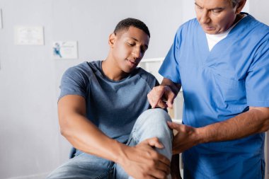 Olgun kayropraktik uzmanı, klinikteki Afrikalı Amerikalı bir adamın yaralı dizini işaret ediyor.