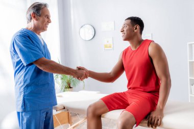 Spor giyim bölümünde, klinikte kayropraktik uzmanıyla tokalaşan mutlu Afrikalı Amerikalı adam. 