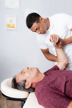 Afrikalı Amerikalı kayropraktik uzmanı klinikte orta yaşlı bir adamın kolunu düzeltiyor.