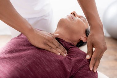 Genç Afrikalı Amerikalı masör masaj masasında orta yaşlı bir adama masaj yapıyor.