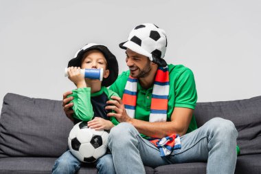 Futbol fanatiği şapkalı mutlu bir adam, sarılan bir çocuk.