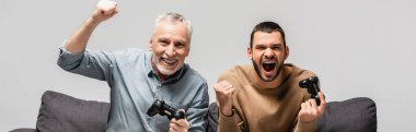 KYIV, UKRAINE - 17 Kasım 2020: Gri, sancak üzerinde kumandalı joystickleri tutarken yetişkin oğlu olan heyecanlı adam zafer jesti gösteriyor