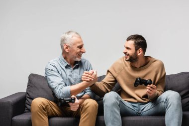 KYIV, UKRAINE - 17 Kasım 2020: neşeli baba ve oğlu gri üzerinde izole edilmiş joystickleri tutarken el sıkışıyor