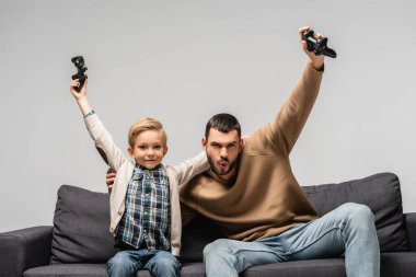 KYIV, UKRAINE - 17 Kasım 2020: Heyecanlı adam ve mutlu çocuk, gride izole edilmiş joysticklerle galibiyet jesti gösteriyor
