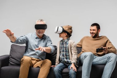 KYIV, UKRAINE - 17 Kasım 2020: yetişkin bir adam vr kulaklığıyla hareket ediyor torun ve oğlu ile joystick gri üzerinde izole