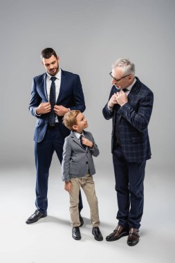 smiling businessman looking at grandfather and grandson touching ties on grey clipart